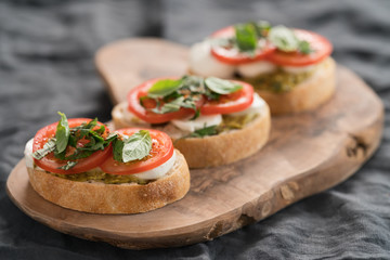 Bruschetta with mozzarella, tomatoes and basil with pesto on olive wood board