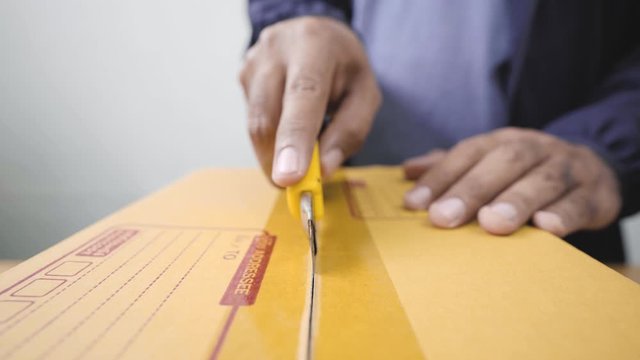 Close Up. Fast post shipment service concept. young asian man customer opening and cutting parcel cardboard box at home office desk. 4K Resolution.