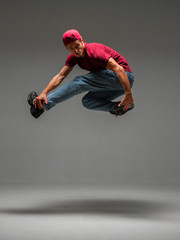 Cool young guy breakdancer jumps dancing hip-hop isolated on gray background. Dance school poster. Break dance lessons