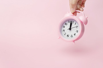 A hand holds alarm clock. A concept of the time and new technologies. Light pink background.