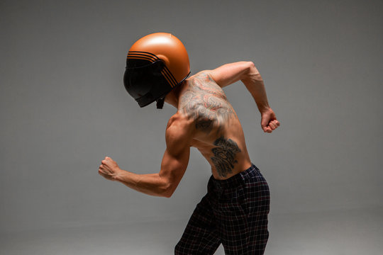 Handsome guy racer in helmet runs on grey background in studio. Kart racing school poster. Body with tattoo