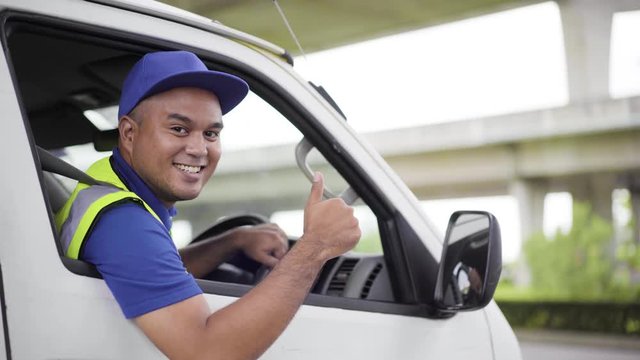 Fast post shipment service concept. Young asian deliveryman wear blue cap sitting in van thumbs up to camera and smile. 4k Resolution.