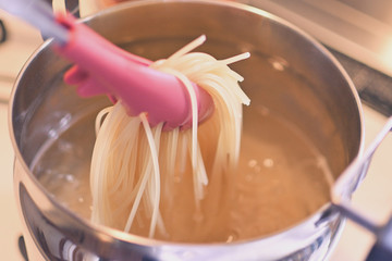 お鍋にお湯を沸かし、スパゲッティーの麺を茹で、トングで持ち上げたところ