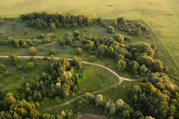 Aerial view of rural road between green field and forest.