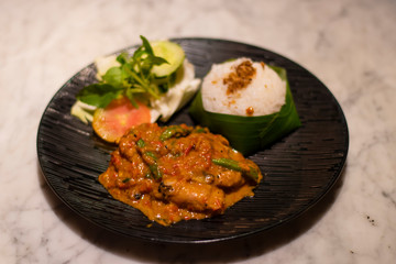 Decorated platter dinner with creamy chicken, rice and salad served in a black plate on a table in touristic visit in Bali