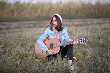 Young European woman or student is sitting with a guitar in the evening in a field