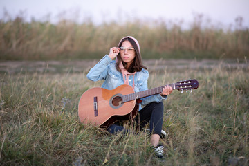 Young European woman or student is sitting with a guitar in the evening in a field