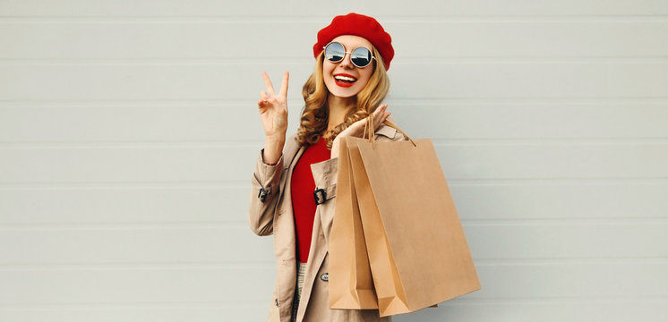 Autumn portrait of attractive smiling woman with shopping bag wearing a coat, red french beret over gray background