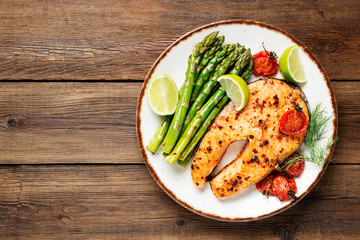 Baked salmon steak garnished with asparagus and tomatoes .