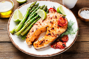 Baked salmon steak garnished with asparagus and tomatoes .
