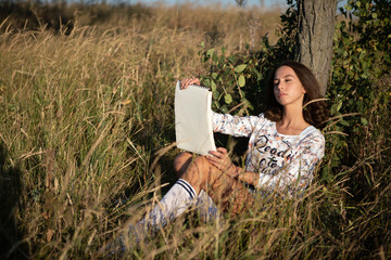 Young European woman or student is drawing in the evening outdoor in a field