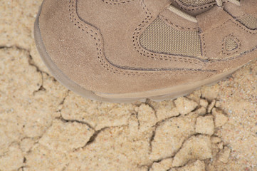 Brand new suede and nylon beige tan camo military tactical desert combat boot, arid dried soil and sand, detailed horizontal background macro close-up, bare earth, dust, pebbles rough terrain off-road