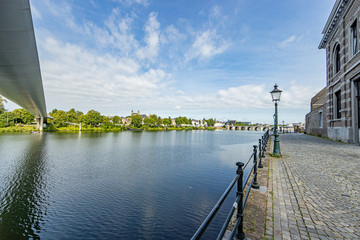 Sidewalk with pole lamps and metal fence, Maas river with the High Bridge, the St. Servatius Bridge (Sint Servaasbrug) and the center of Maastricht in the background in South Limburg, Netherlands