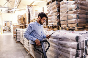 Young attractive smiling supervisor pushing forklift and holding tablet to check on goods for...