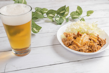 光が差し込むテーブルに置かれた、冷えたビールと豚キムチ