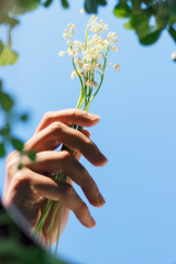 Reflection in the mirror. A woman's hand holds a bouquet of lilies of the valley. Blue sky. Background, texture. Lifestyle