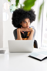Thoughtful young African American teen girl student with Afro hair using laptop looking through...