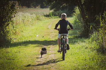 Fototapeta premium a boy rides a bicycle and a little black dog runs beside him