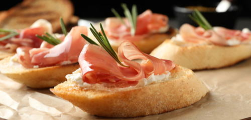 Tasty bruschettas with prosciutto and cream cheese served on table, closeup. Banner design