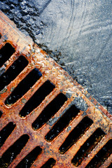 Rusty grate of storm sewers during the rain. Urban drainage system in action. Vertical photo