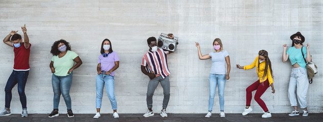 Happy friends wearing face mask listening music with vintage boombox outdoor - Multiracial young people having fun dancing together during corona virus outbreak - Youth millennial friendship concept - obrazy, fototapety, plakaty
