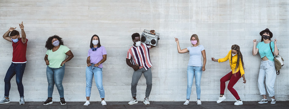 Happy friends wearing face mask listening music with vintage boombox outdoor - Multiracial young people having fun dancing together during corona virus outbreak - Youth millennial friendship concept