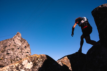 A trail runner silhouetted against a bright blue sky while climbing a mountain. - 371754929