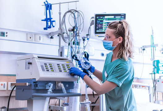 COVID19 / 2019-ncov concept: nurse, wearing a surgical mask, checks the settings of a mechanical ventilation machine, which is seen in the foreground. therapy used for lung breathing