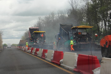 Suburban highway road repair works, asphalt compactor paver machines with smoke and workers people in signal coveralls protective special clothing at cloudy autumn day