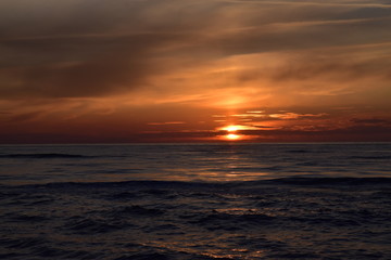 Naklejka na ściany i meble Zachód słońca nad morzem z falami w odcieniach mocnego pomarańczu i czerwieni. 