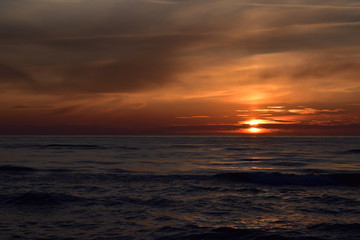 Fototapeta na wymiar Zachód słońca nad morzem z falami w odcieniach mocnego pomarańczu i czerwieni. 