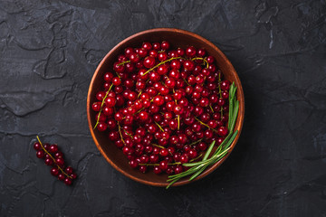 Fresh sweet red currant berries with rosemary leaves in wooden bowl, dark textured background, top view
