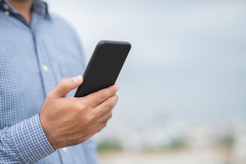 Close up male hands holding using black smartphone on city background.
