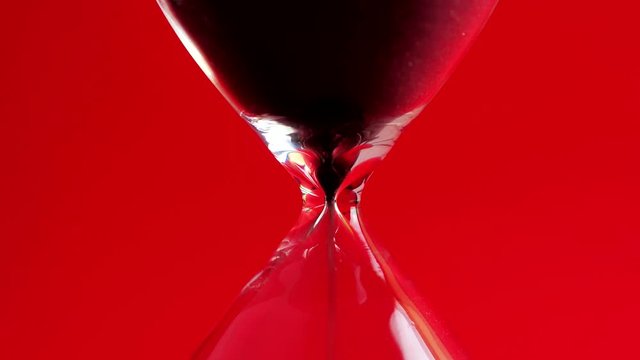 Close up pouring black sand in an hourglass standing an rad background 4k