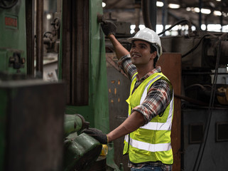 Portrait of young handsome technician man or industrial worker with hard hat or helmet and vest jacket working electronic machinery and mechanical engineering in Factory of manufacturing place