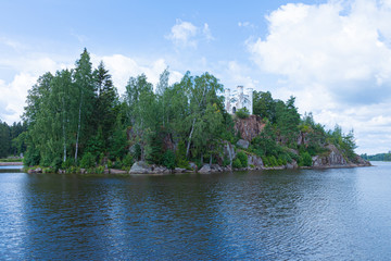 Old alone fortress, little castle, lighthouse or beacon on cliff or mountain with green fortress on the island among ocean, sea, lake water with waves  in clear sunny summer days