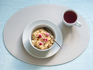 Breakfast with quinoa porrige and cup of hot herbal tea on tabletop. Bowl wit quinoa milk porridge with berries and almond over blue linen tablecloth. Top view or flat lay. Copy space