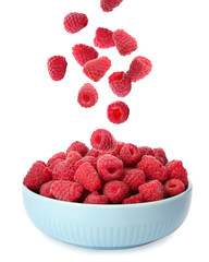 Fresh ripe raspberries falling into bowl on white background