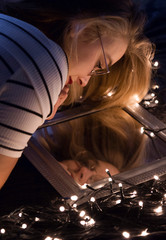 Abstract Selfportrait of a young woman with glasses looking at her reflection in a mirror surrounded by fairylights.