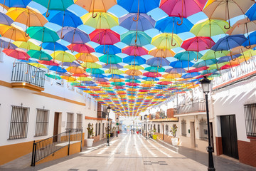 The sky is full of colorful umbrellas. Street with umbrellas in the sky in the village San Bartolome de la torre. Summer decoration and sun  protection. Huelva province, Andalusia, Spain