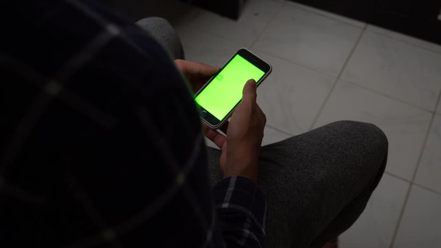 4K - OTS shot of a man scrolling on his phone with a green screen. Shady man scrolling through his mobile. 