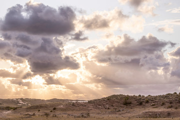 Sun peeking through the clouds above dune landscape
