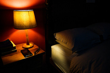 Cozy scene of a bed with pillows, a bedside lamp with shade, a mobile phone and reading glasses