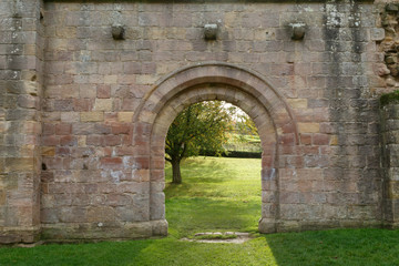 Fototapeta na wymiar Gothic Archway Leading to an Open Field with a Tree, Fountains Abbey, Ripon, North Yorkshire, England, UK.