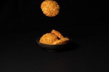 fried crispy rice crackers called rice age with soy,salt sugar etc flavor on black background is a traditional japanese snack.