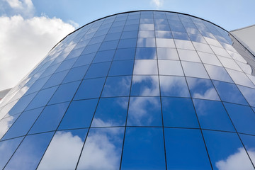 Plakat glass facade of a modern office building against a blue sky with clouds