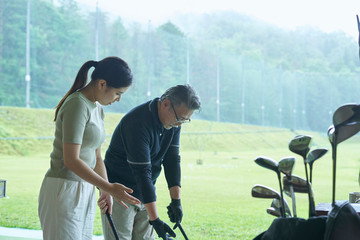 ゴルフ場でゴルフを教える男性と教わる女性