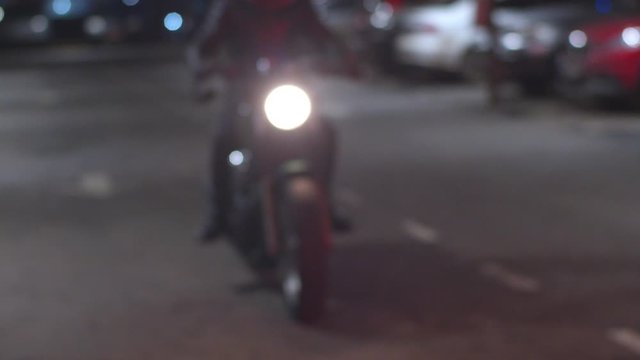 Slow-motion of biker in helmet riding bike in parking lot, garage building. Motorcyclist stops near camera with motorbike light shot getting blurred, man return home and park his motorcycle at night