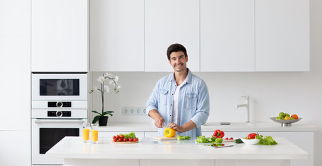 Happy young man preparing cooking healthy vegan food cut salad in kitchen.