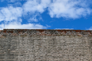 Old brick wall. Blue sky background with clouds. Red brick, white paint.